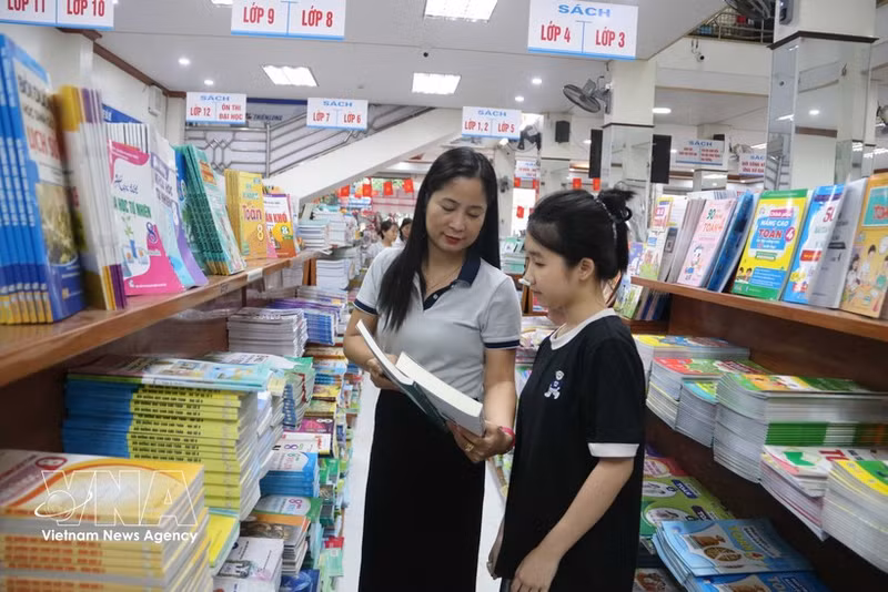 새 학년을 앞두고 딸이 사용할 교과서를 고르는 어머니. (사진: VNA)