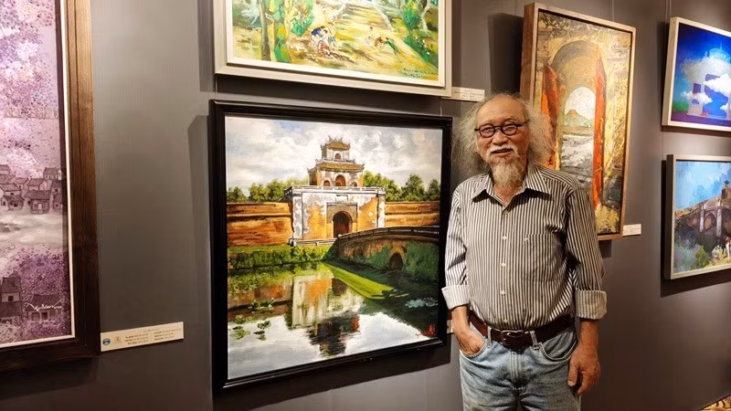 당 머우 뜨우 화가가 전시회에 전시된 자신의 그림 옆에서 포즈를 취하고 있다.